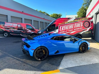 mobile tire service for a blue sports car with Extreme Tires vans in the background; the mobile tire shop serves Sunrise, Broward, Miami, Boca, and Palm Beach, FL