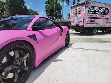 Pink sports car in driveway with closeup of tires and wheels installed and the Extreme Tires  mobile tire and wheel service van in the background